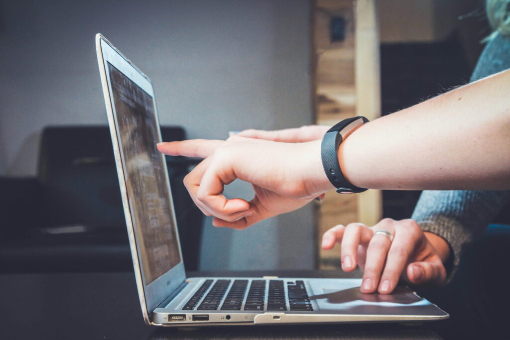 A close-up of hands interacting with a laptop, focusing on one finger pointing at the screen while the other hand types.